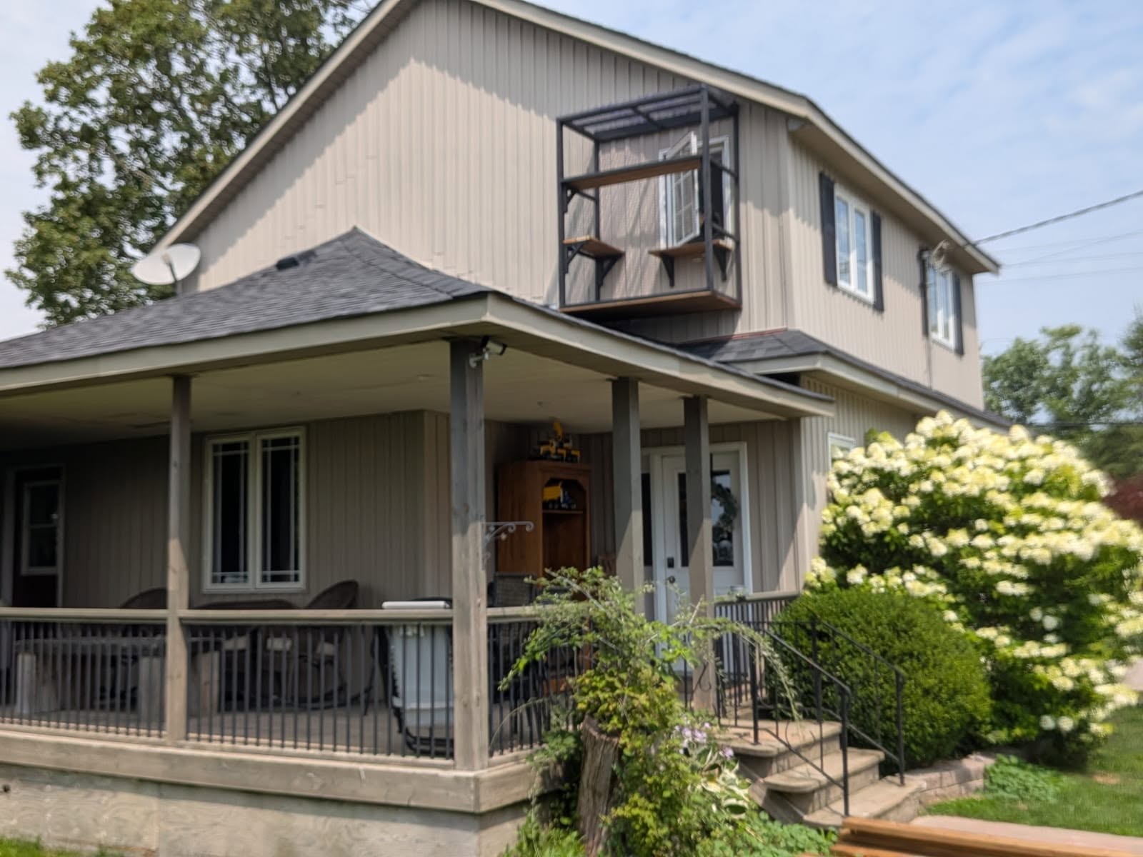 Two-storey house with a small black catio fixed outside an upstairs window, above a wraparound porch