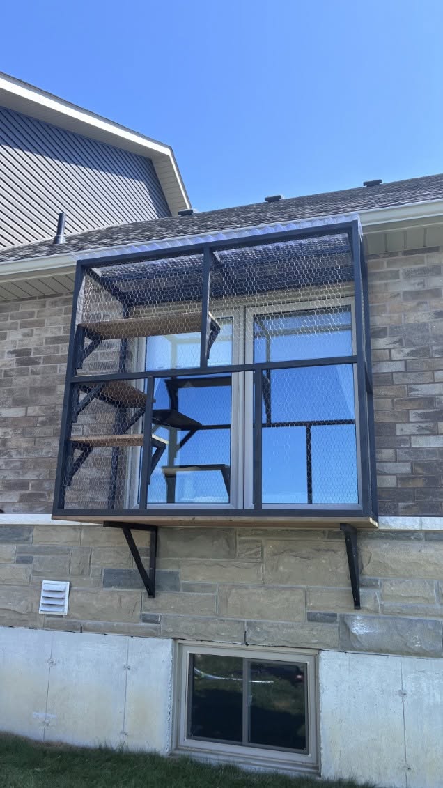 Tall black window box catio on a brick house, with shelves stepping up past the window